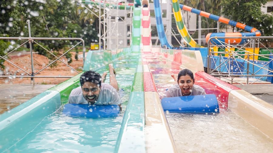 Two people joyfully sliding down a colorful water slide on mats at Black Thunder Water Theme Park.