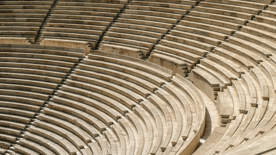 A close-up view of curved, tiered stone seating in an empty amphitheater, showing the symmetrical arrangement and steps between rows.