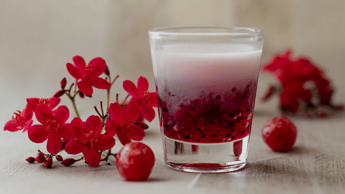a glass with falooda kept on a table with fruits and buds of flowers kept next to it