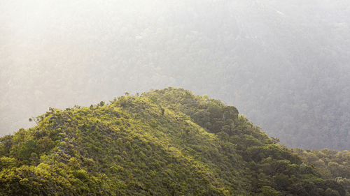 An overview of a hill with sunlight hitting it with another hill in the background