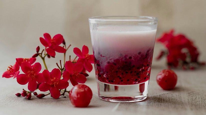 a glass with falooda kept on a table with fruits and buds of flowers kept next to it