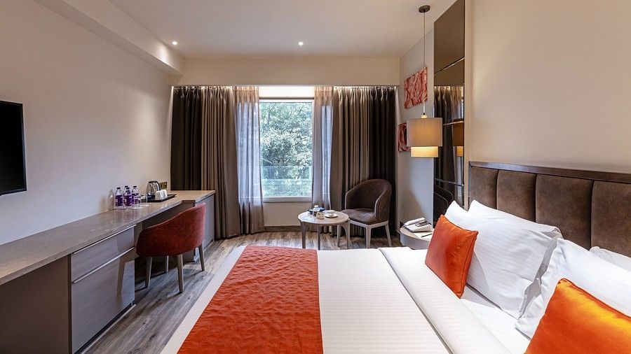 A bedroom view with a window on one side with brown curtains and bed has head rest for a comfortable rest.