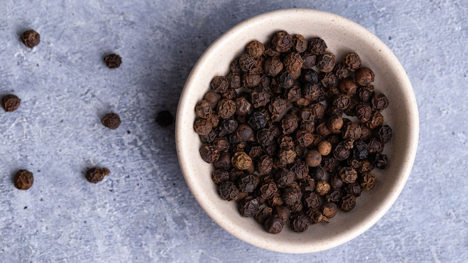 a bowl full of black pepper seeds with other small seeds kept outside for decoration
