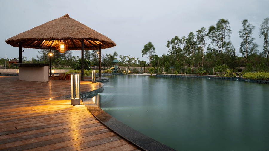 A wooden deck and a thatched-roof gazebo next to an outdoor swimming pool at dusk at Hotel Sonar Bangla, Sundarban. 