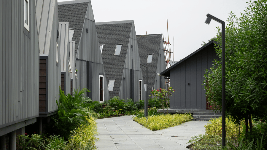 Exterior view of a paved walkway showing the the A-frame style cottages, surrounded by planting beds at Hotel Sonar Bangla, Taki.