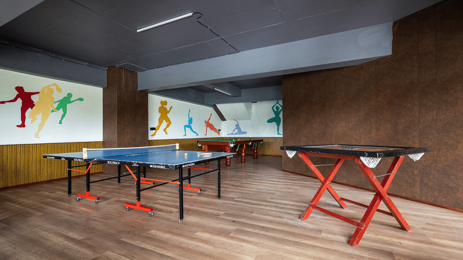 Indoor recreation room with wooden flooring, two table tennis tables, and brown and black walls at Hotel Sonar Bangla, Taki.