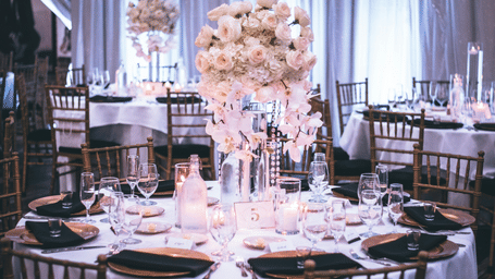 Elegantly set round tables with floral centrepieces in a banquet hall, with long white curtains draping the background