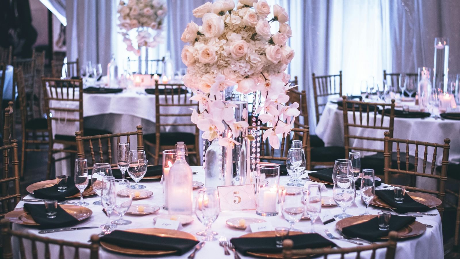 A banquet hall is set with floral centrepieces, elegant tableware, and dark wood chairs.