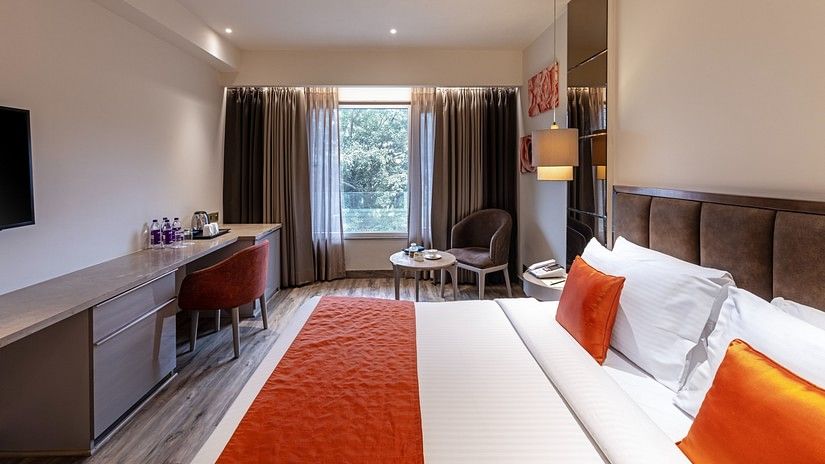 A bedroom view with a window on one side with brown curtains and bed has head rest for a comfortable rest.