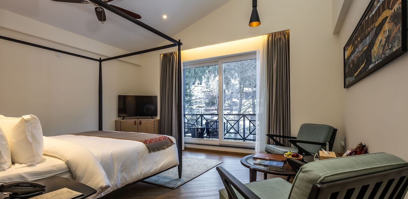 Bedroom with a four-poster bed, seating, and balcony area with mountain views at Nivasana Manali.