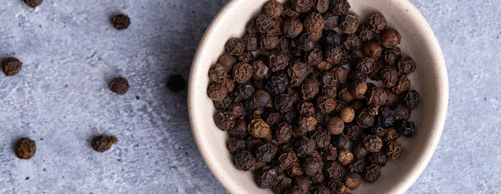 a bowl full of black pepper seeds with other small seeds kept outside for decoration