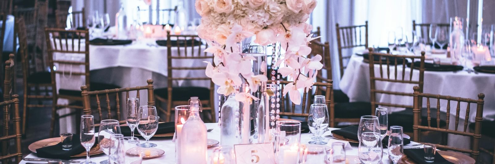 A decorated banquet hall with elegantly set dining tables and floral centrepieces.