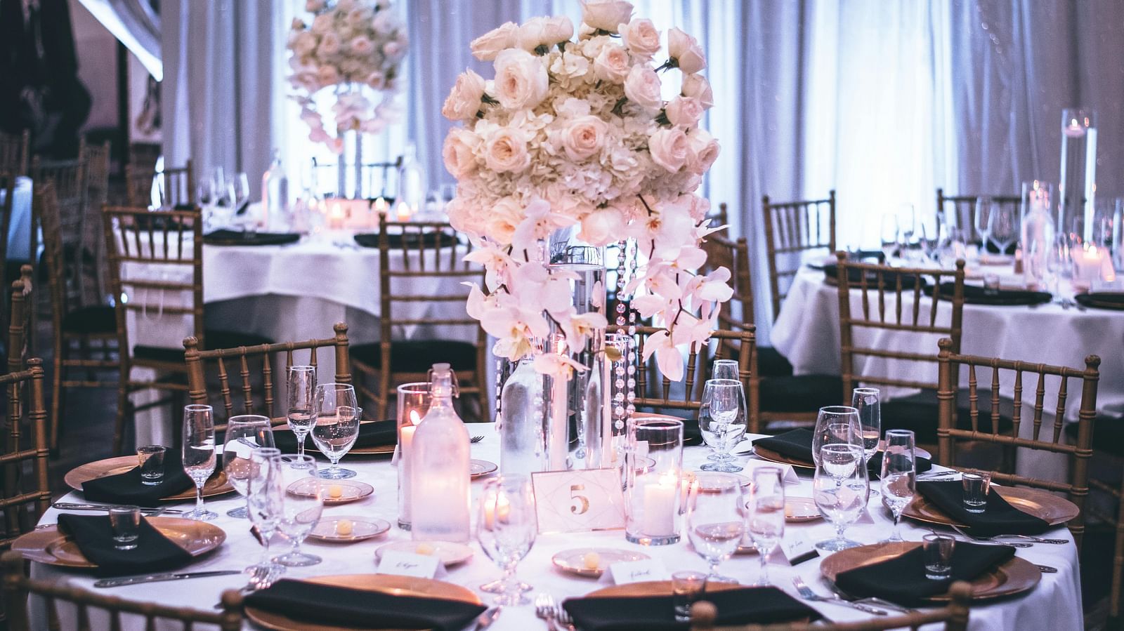 A banquet table set for an event with elegant golden chairs, crystal glassware, white flowers centerpiece, and candles.