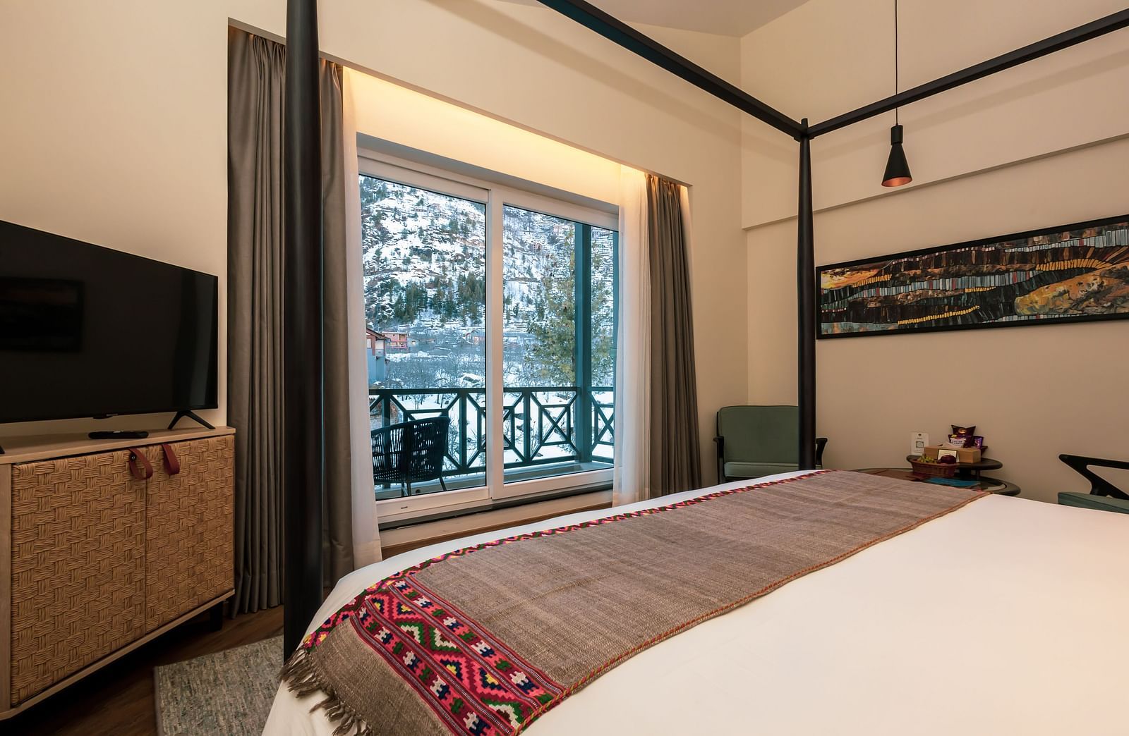 A room with a four-poster bed, television, and balcony offering snowy mountain views at Nivasana Manali.