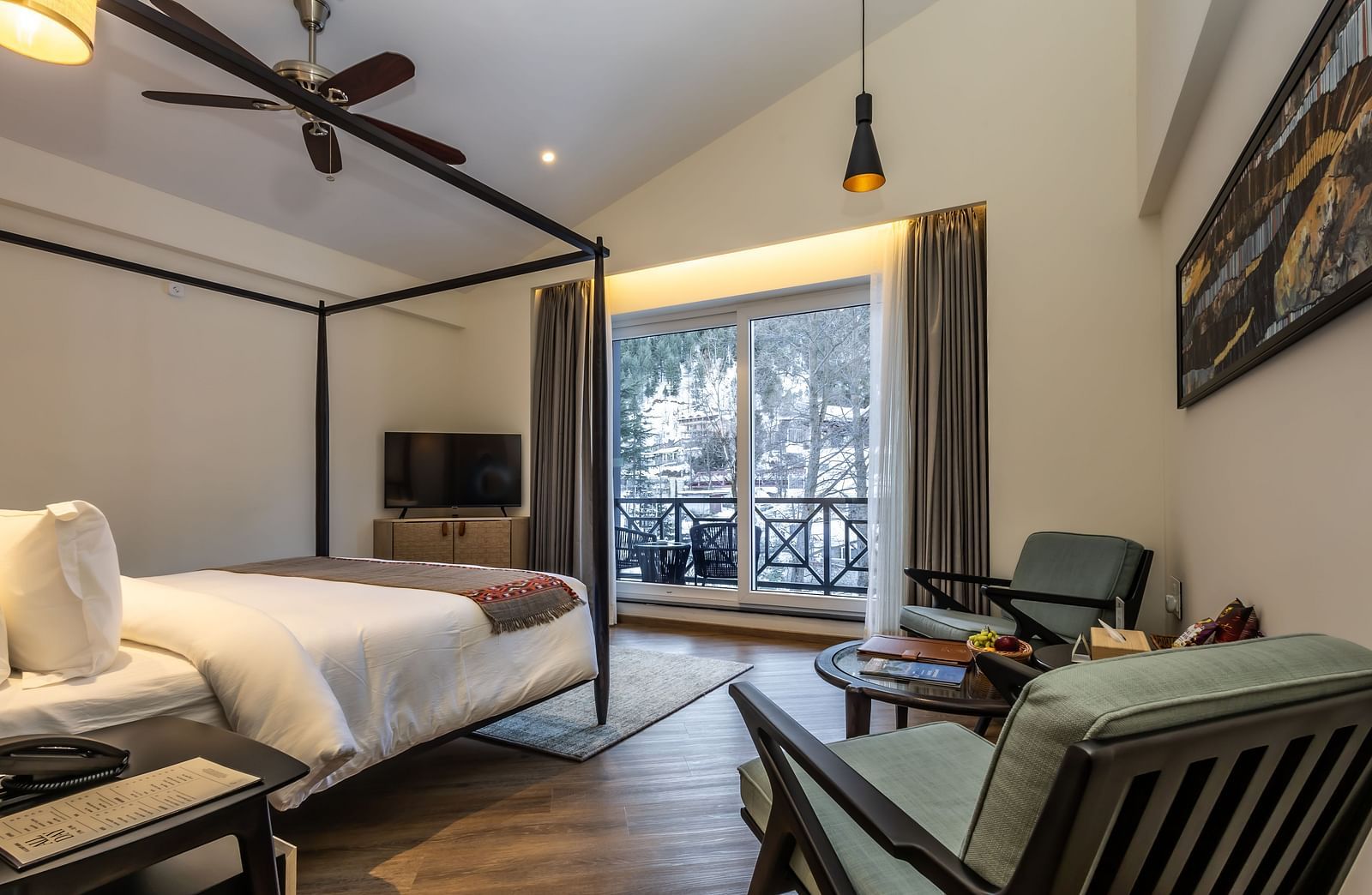 Bedroom with a four-poster bed, seating, and balcony area with mountain views at Nivasana Manali.