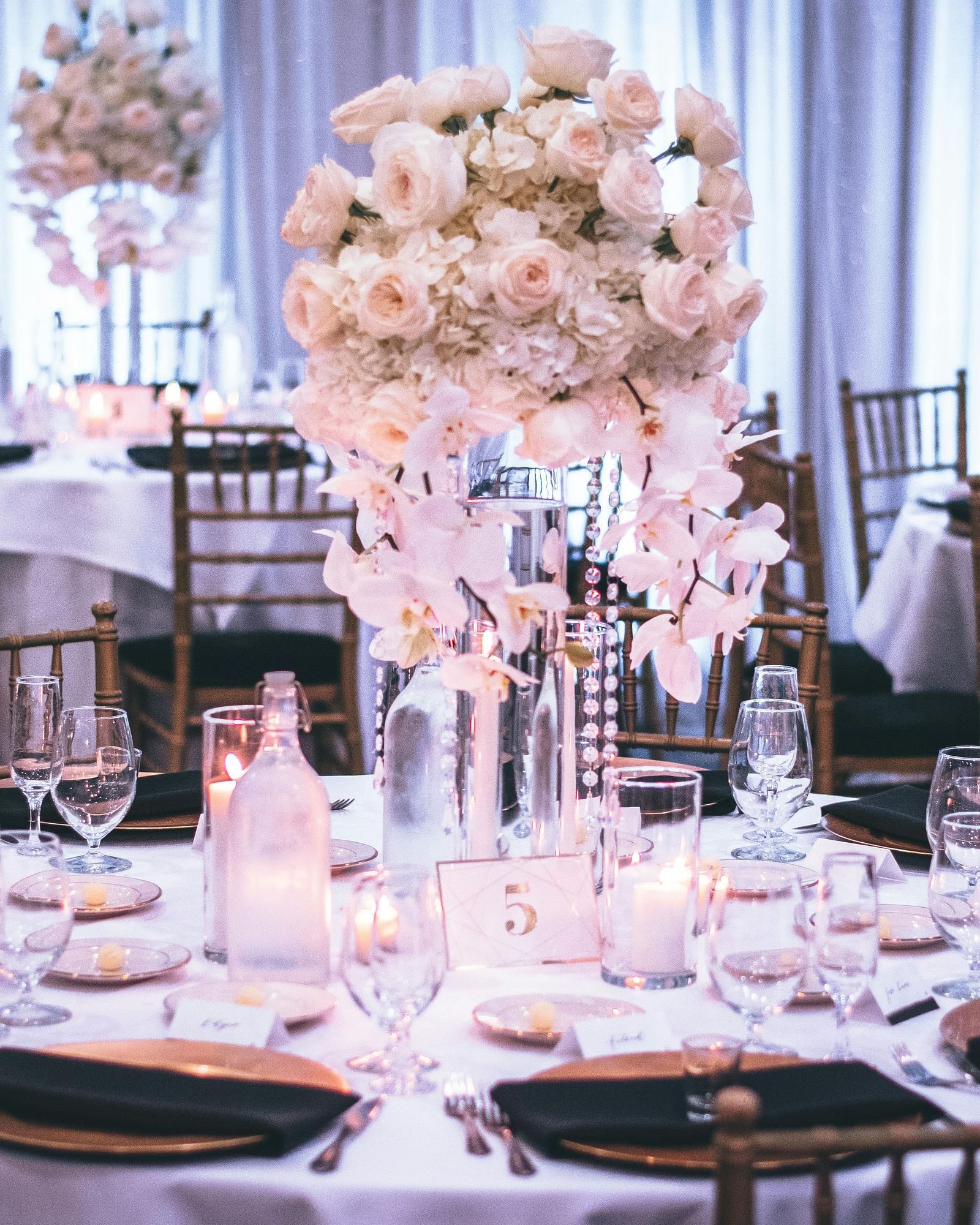 Elegantly set round tables with floral centerpieces await guests in a banquet hall at Lords Plaza Surat.