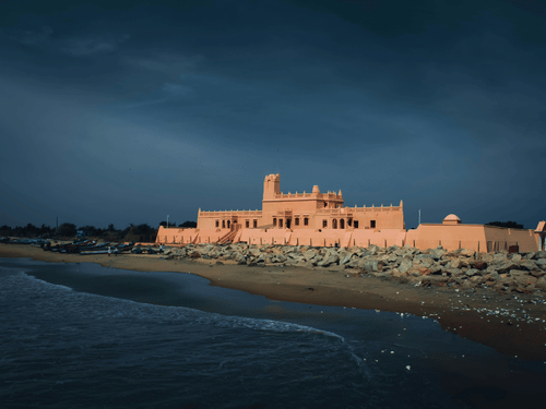 A tan stone building situated on a dark beach under a moody, overcast twilight sky.