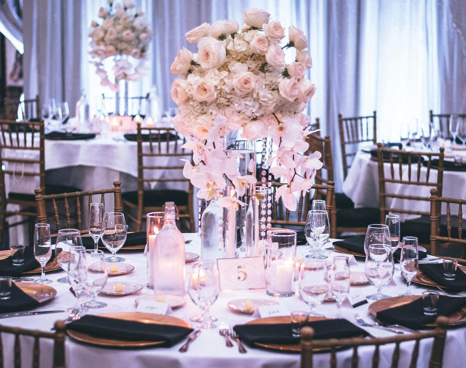 A banquet hall is set with floral centrepieces, elegant tableware, and dark wood chairs.
