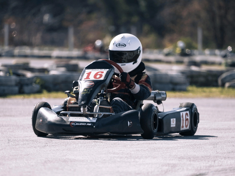 A person wearing a helmet go-karting on an outdoor track, with black tyres in the background.