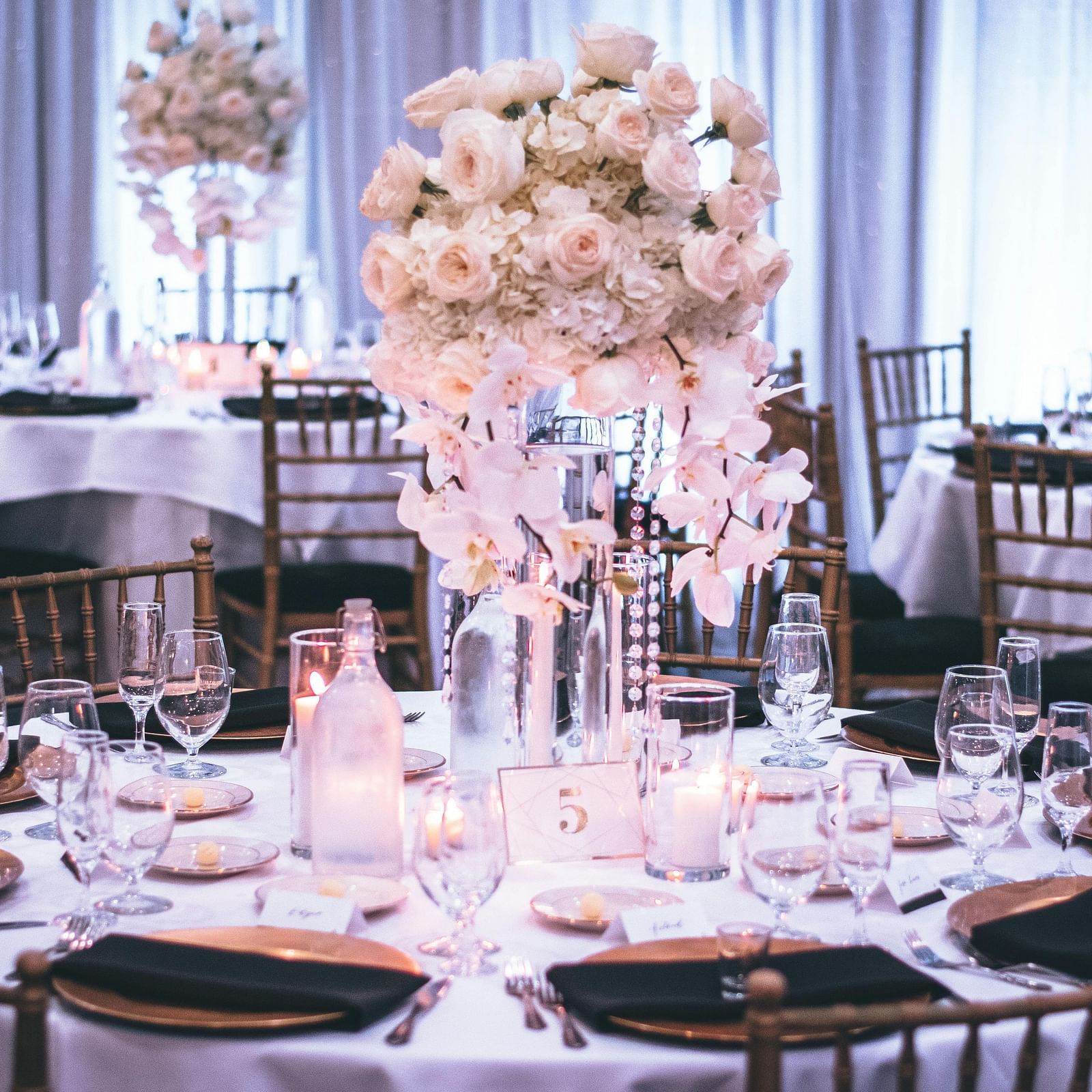Elegantly set round tables with floral centerpieces await guests in a banquet hall at Lords Plaza Surat.