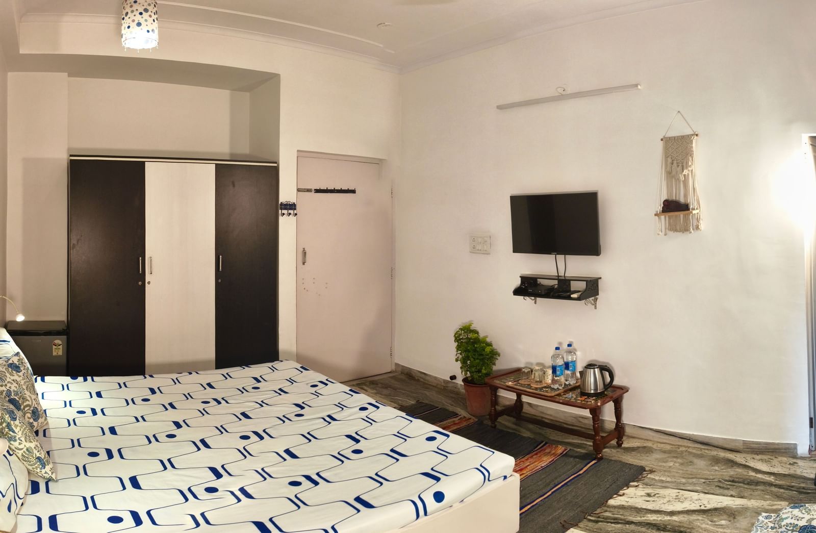 A modern bedroom with a double bed, white and blue bedsheet, TV unit, small table and seating area at Jaypore360 Homestay - Best Rooms in Jaipur.