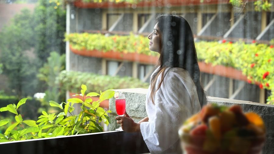 A woman in a robe enjoys a drink while enjoying in the rain, with a bowl of fresh fruit and greenery in the background