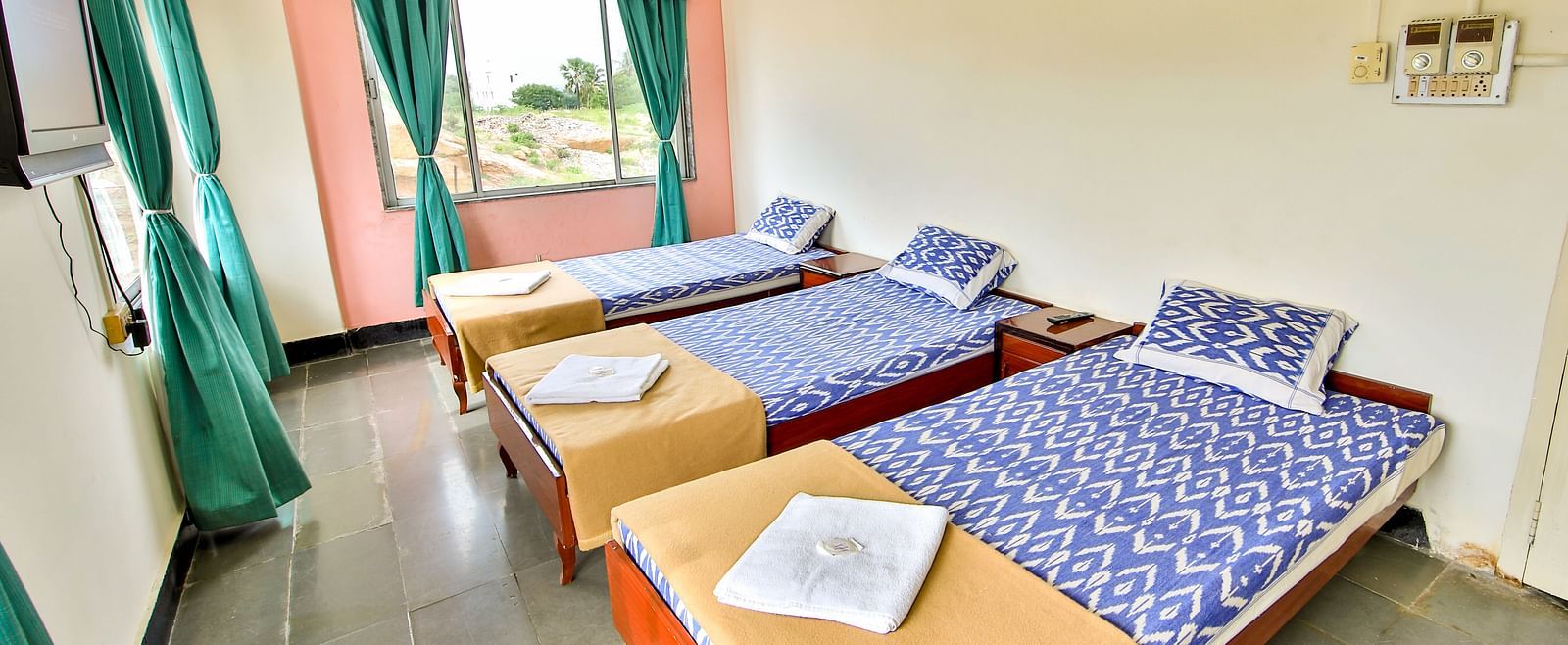 A side view of two beds with bedding in a room with a window and TV at Hotel Sahara - Cozy Room in Ramoji Film City, Hyderabad.