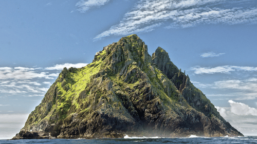 A solitary island with a mountain and greenery covering it with blue sky in the backrgound