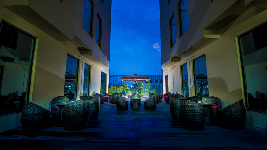 Atmospheric outdoor courtyard seating at dusk, featuring dark woven furniture situated between two modern buildings at Golden Tulip Kukas, Jaipur.
