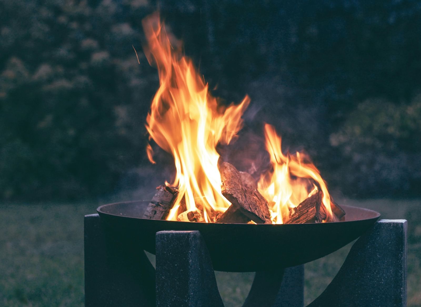 An image of a bonfire lit on a stand with greenery in the background