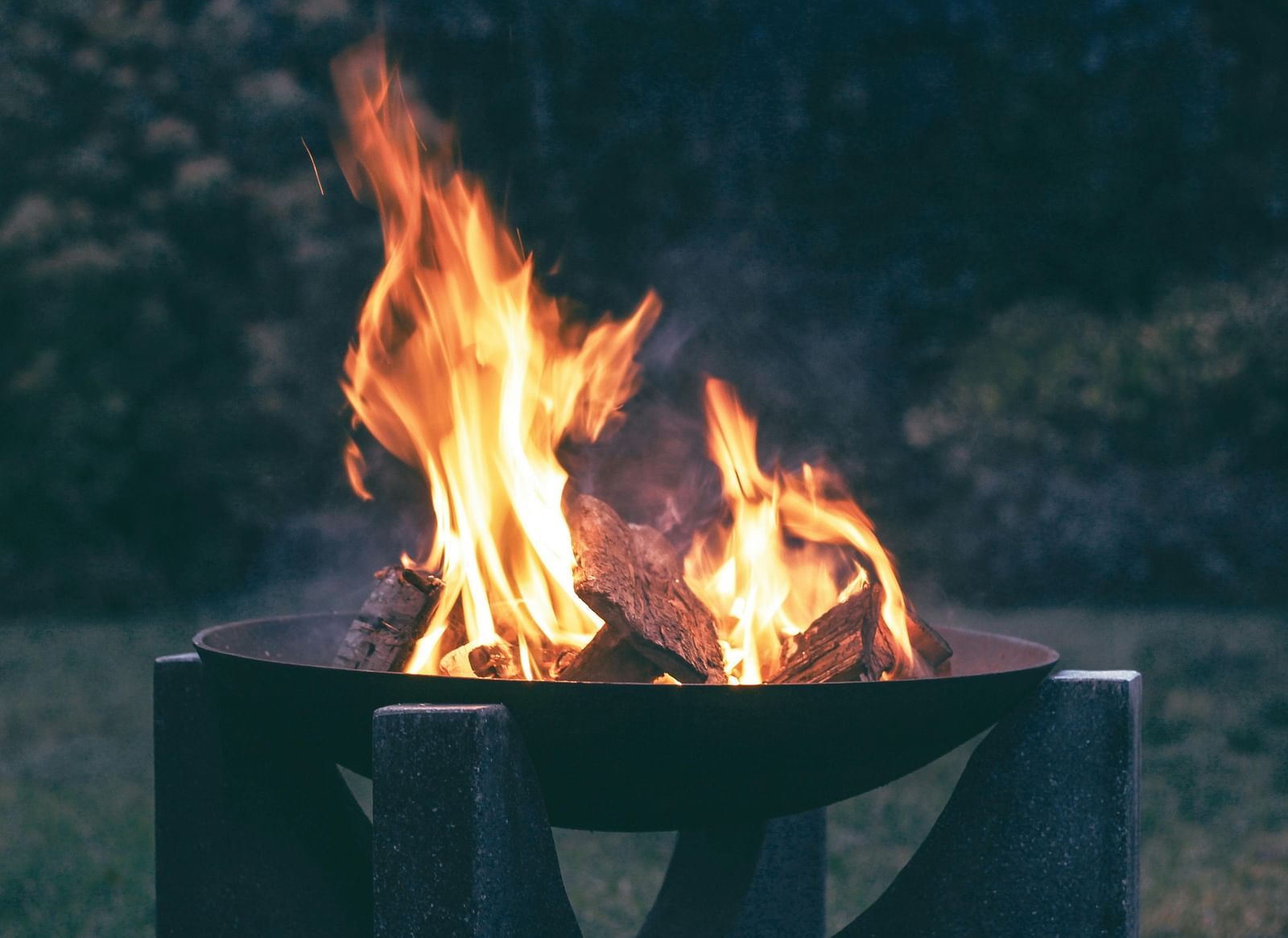 An image of a bonfire lit on a stand with greenery in the background