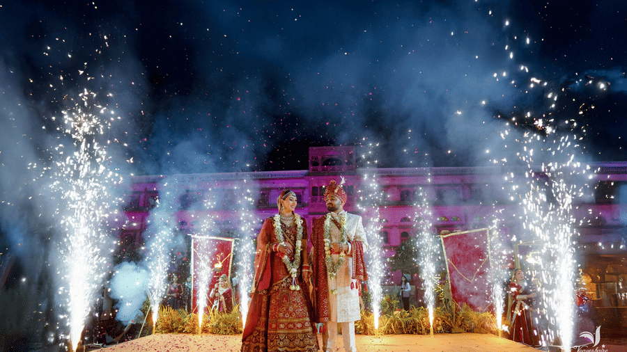 Couple on a decorated wedding stage with fireworks display at night at Umaid Palace.