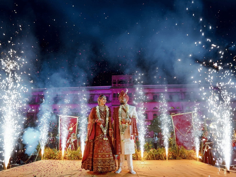 Couple on a decorated wedding stage with fireworks display at night at Umaid Palace.