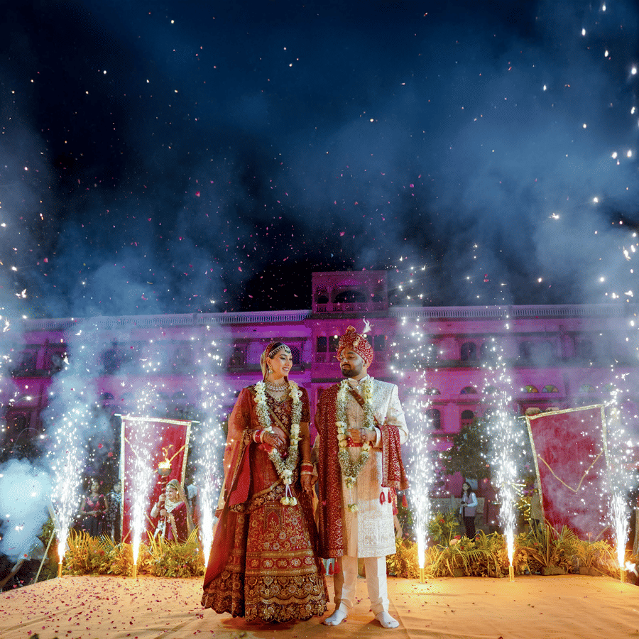 Couple on a decorated wedding stage with fireworks display at night at Umaid Palace.