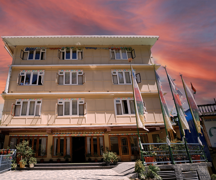 Mount Magnolia Boutique Hotel & Spa in Pelling featuring a pastel-toned multi-storey building with symmetrical windows, entrance garden, and colourful sunset sky backdrop.
