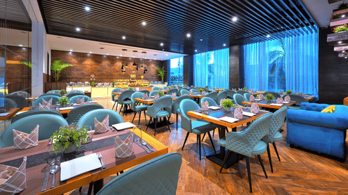 An image of Sumac Restaurant in Agra filled with blue coloured chairs placed in front of tables creating a great ambience for dining - Golden Tulip, Agra