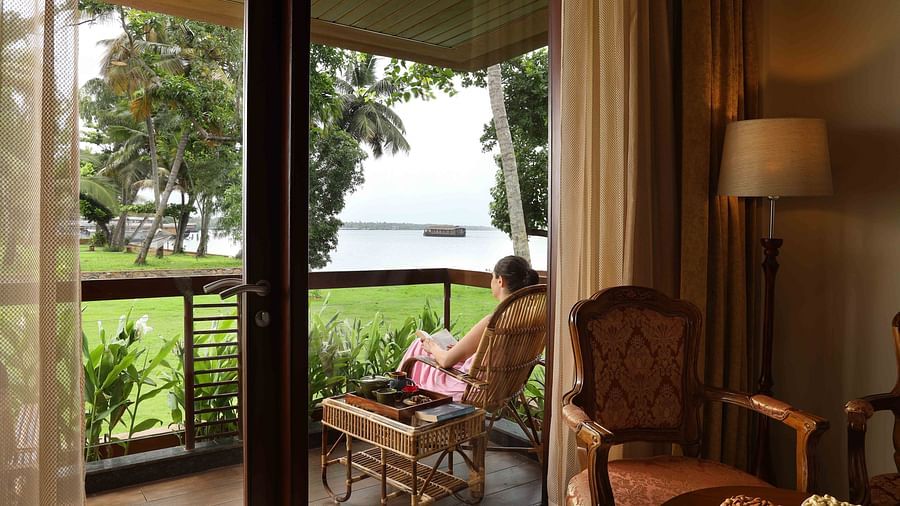 A woman reading a book on the balcony of the Lake View Suite at Uday Backwater Resort, overlooking the tranquil backwaters