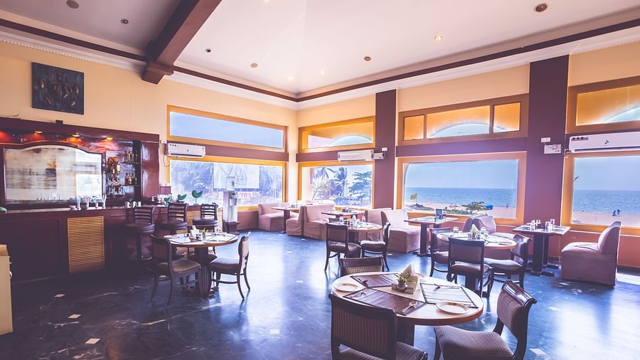 Interiors of a restaurant at Paradise Isle Beach Resort, Udupi with seating arrangement and views of the ocean