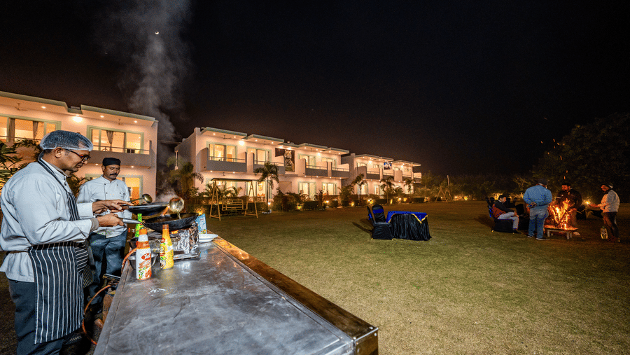 Outdoor cooking at Vedikant Resorts The Mallard Corbett featuring two chefs cooking near a lawn where there is a set up of tables and chairs near the two storey buildings of the property.