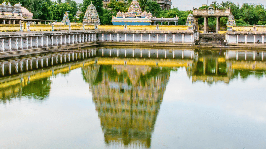 A grand South Indian temple with towering gopurams and a sacred water tank reflecting its intricate architecture.