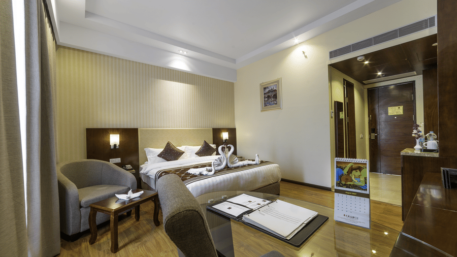 A spacious hotel suite featuring polished wooden floors, a glass dining table, and a grey sofa at Golden Tulip Kukas, Jaipur.