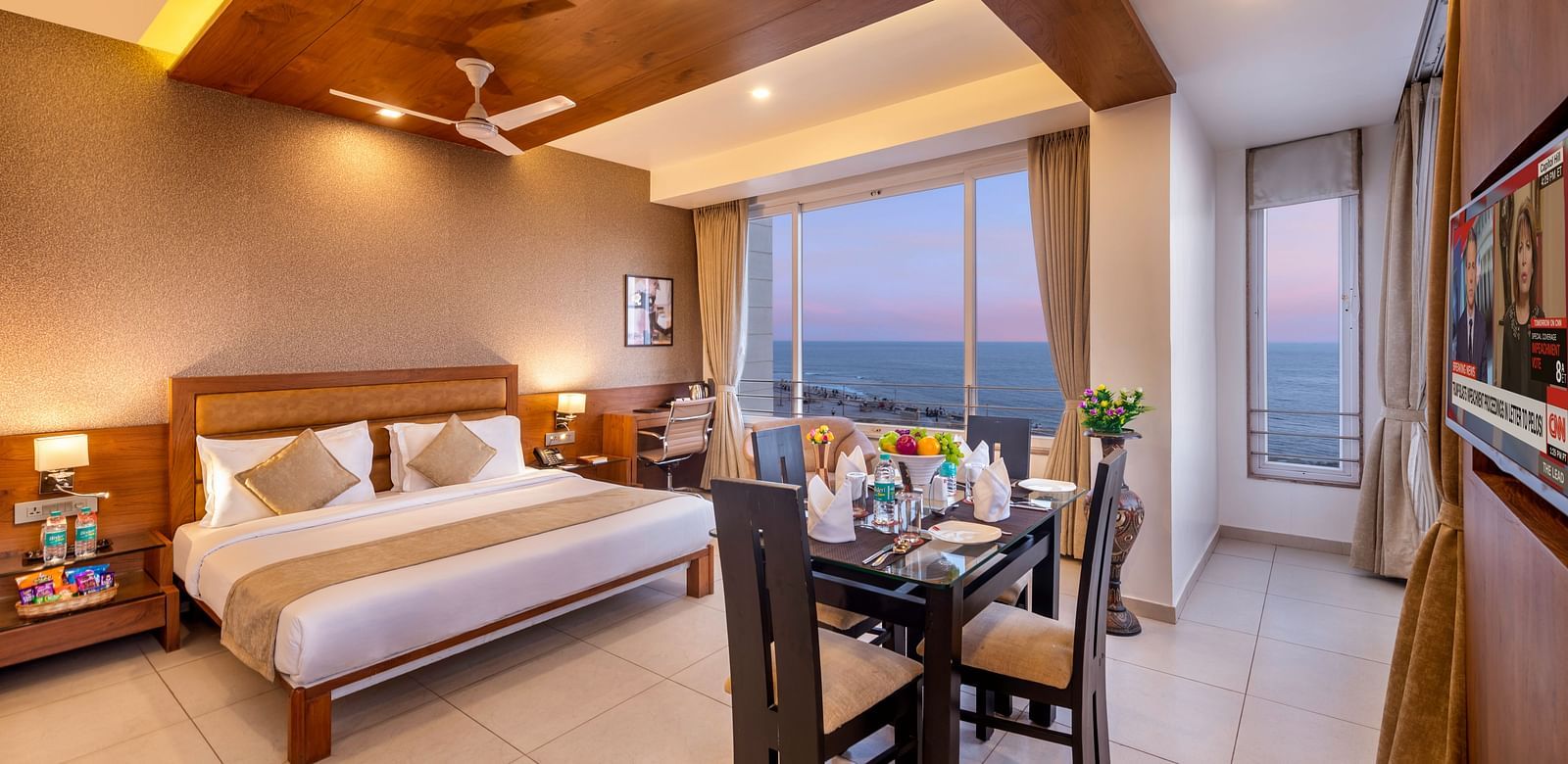 A comfortable hotel room with a bed, dining area, workspace, and a large window offering a view.