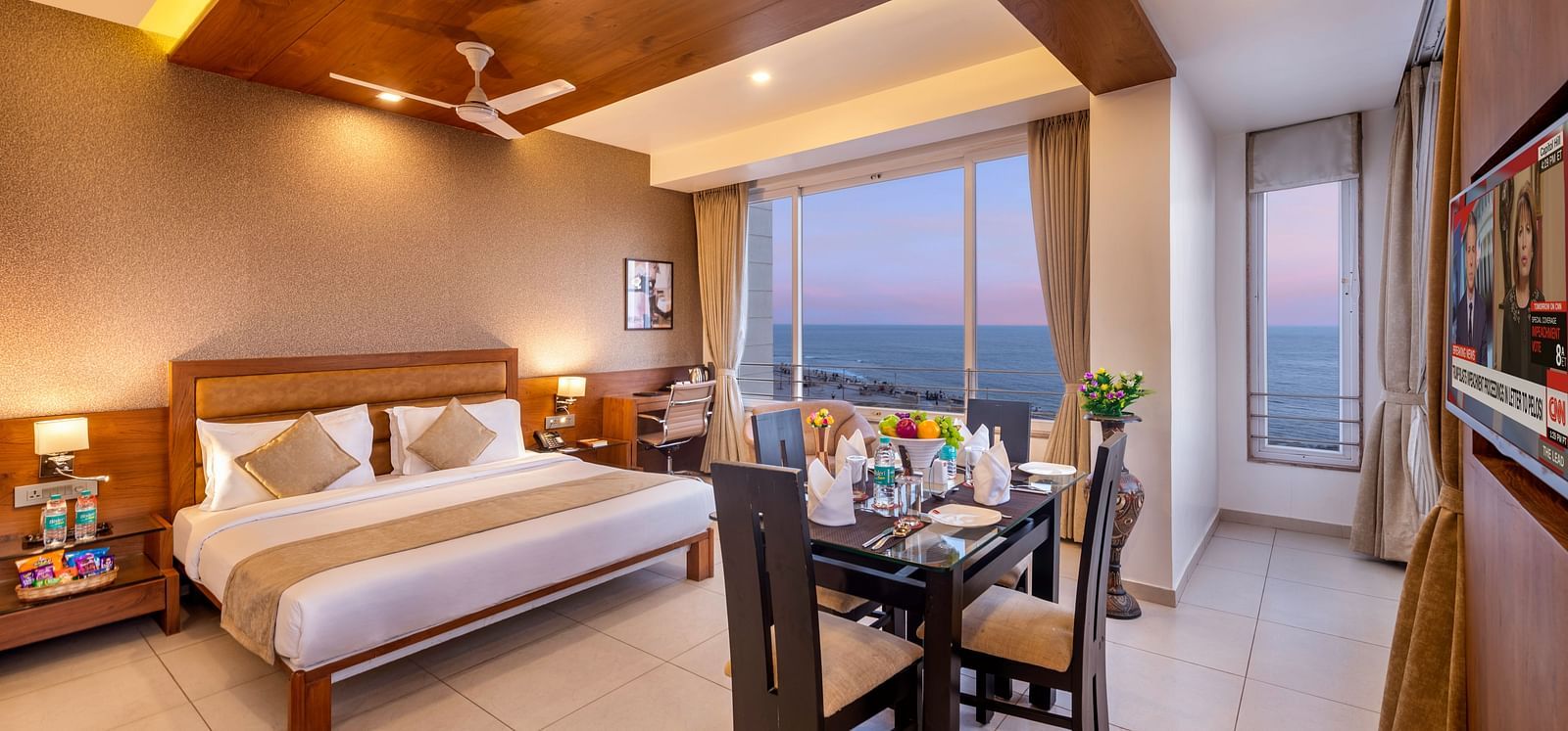 A comfortable hotel room with a bed, dining area, workspace, and a large window offering a view.