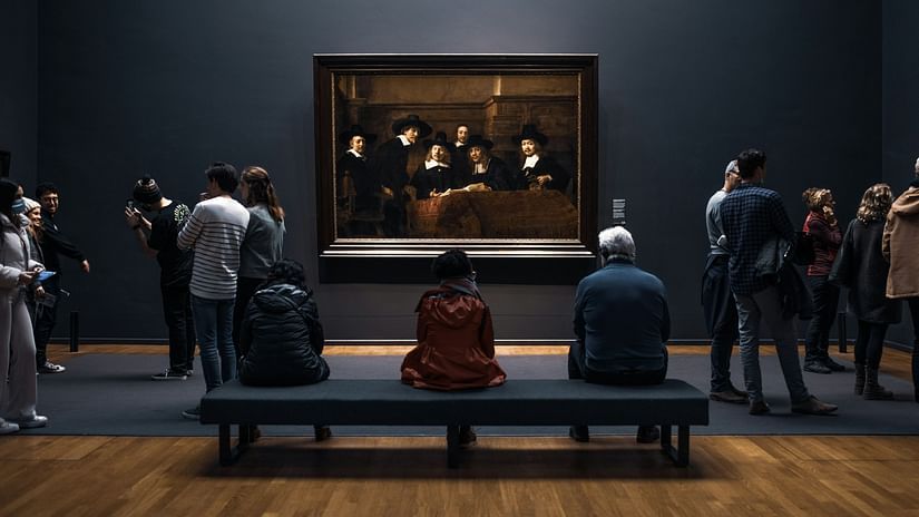 a crowd of people in a lounge talking and looking at a famous painting hung on the wall