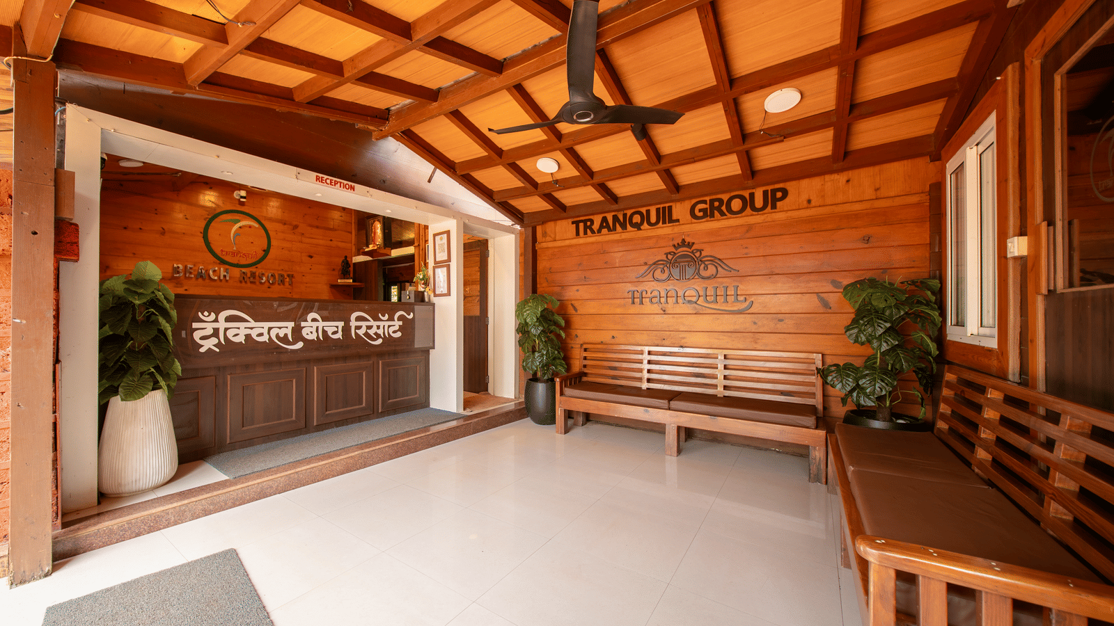 Reception with wooden ceiling, wall art, counter, plant, and welcome sign at Tranquil Beach Resort, Harihareshwar.