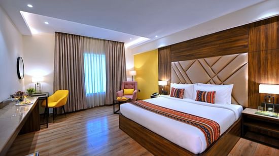 An image showcasing a large bed with a headrest placed in front of a television in our Executive Room in Agra - Golden Tulip, Agra
