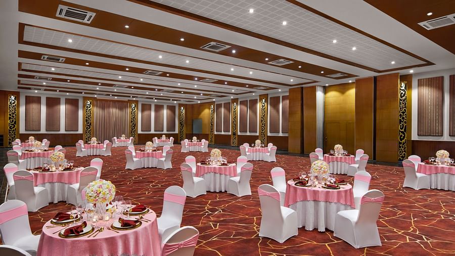 A large ballroom is elegantly set with round tables, pink tablecloths, and white chairs with pink sashes at DGV Resort by Treat, Silvassa