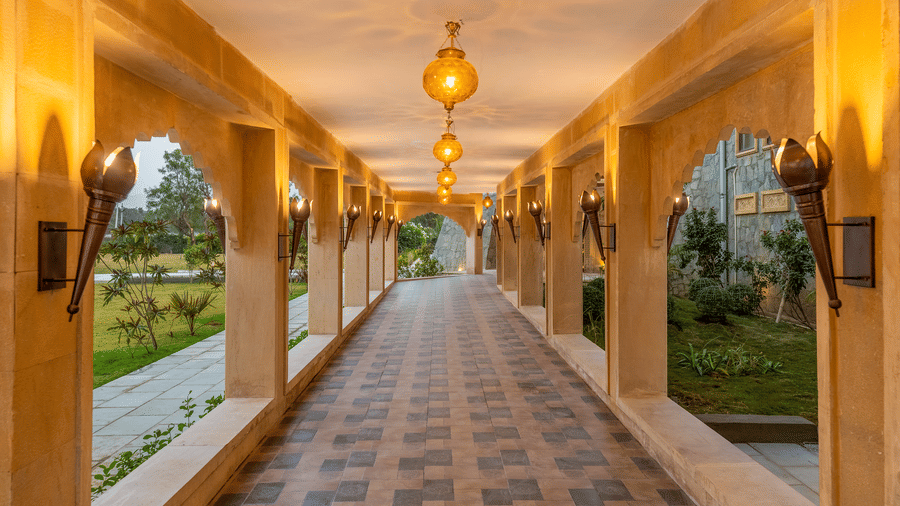 Arched outdoor walkway at EsthereaRaj Leela, Ranakpur with decorative pendant lights and a view of the surrounding resort landscape and greenery.