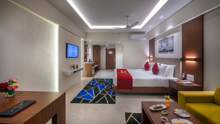 Well-lit hotel room with modern seating, a flat-screen TV, and writing desk - Lords Eco Inn Shapar Rajkot