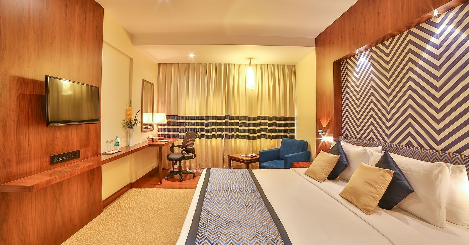 A spacious and modern hotel room with luxurious twin beds, a sofa, and sophisticated interior decor A grand hotel suite with an opulent red and white decor, large bed, and seating area, reflecting a traditional style at Sitara Luxury Hotel in Hyderabad nea